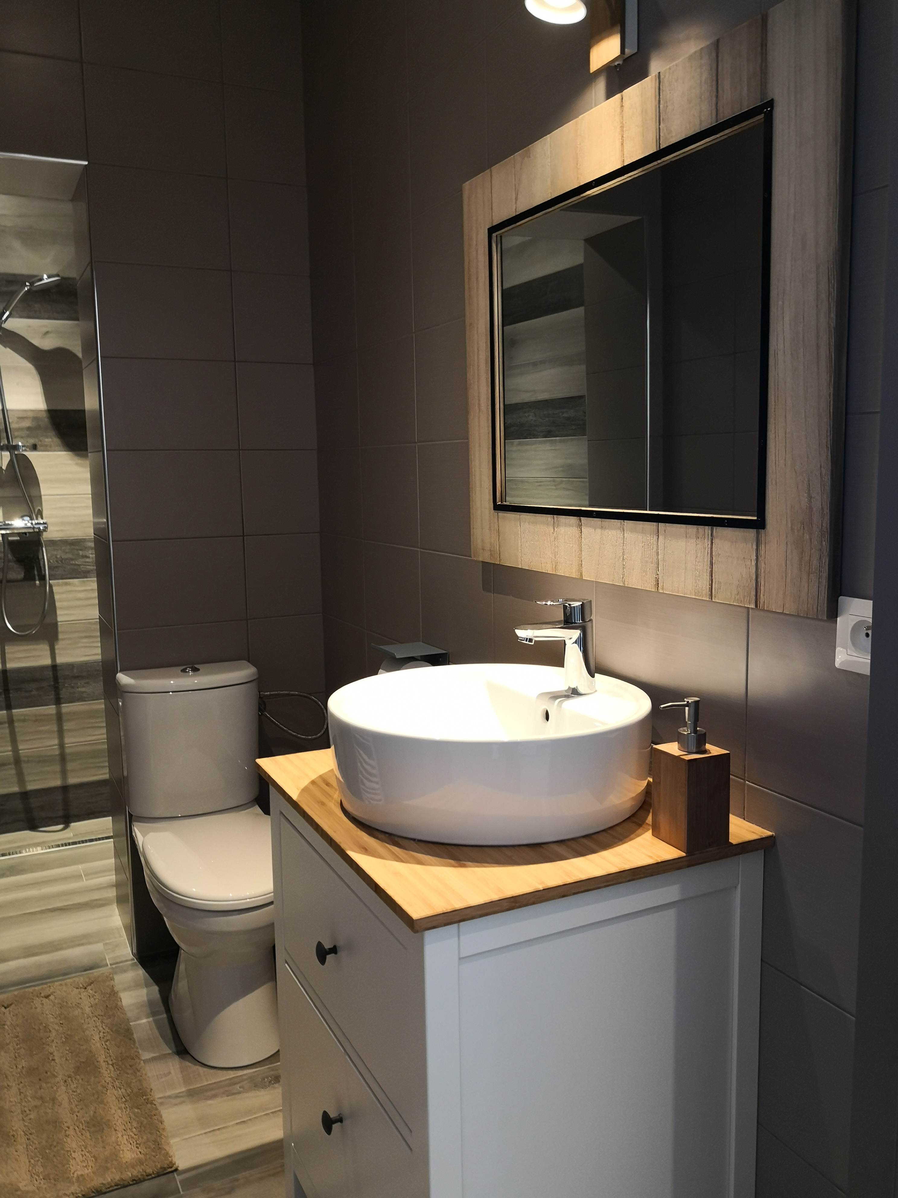 Salle de bain aux murs taupe avec vasque ronde sur plan en bambou, grand miroir à cadre de bois clair et douche à l'italienne.