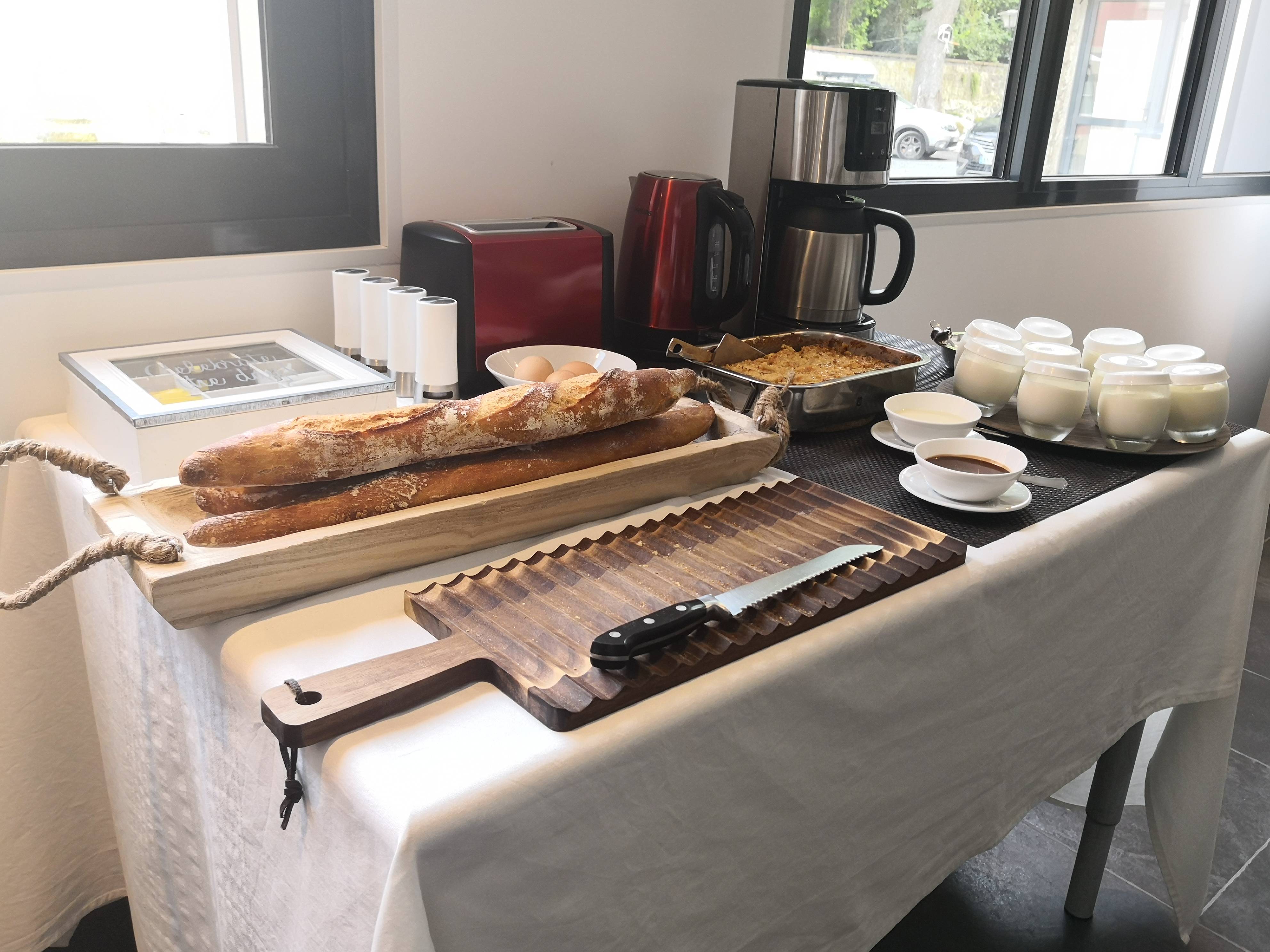 Buffet du petit-déjeuner avec baguettes fraîches sur planche en bois, œufs, gâteau maison et yaourts en pots de verre.